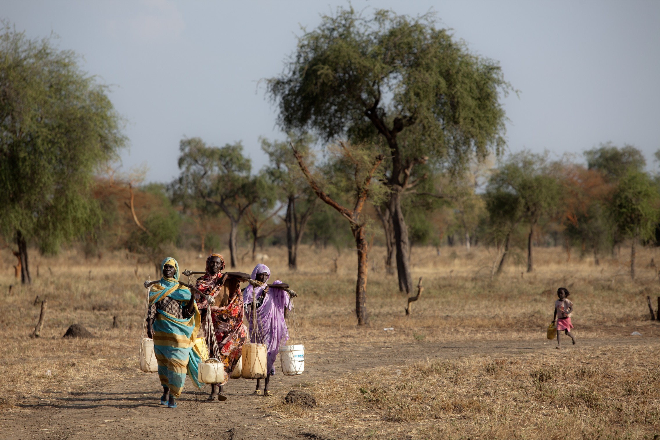 Des femmes transportent de l’eau dans un camp de réfugiés au Soudan du Sud, en décembre 2012. © Fondation Hirondelle / Gwenn Dubourthoumieu